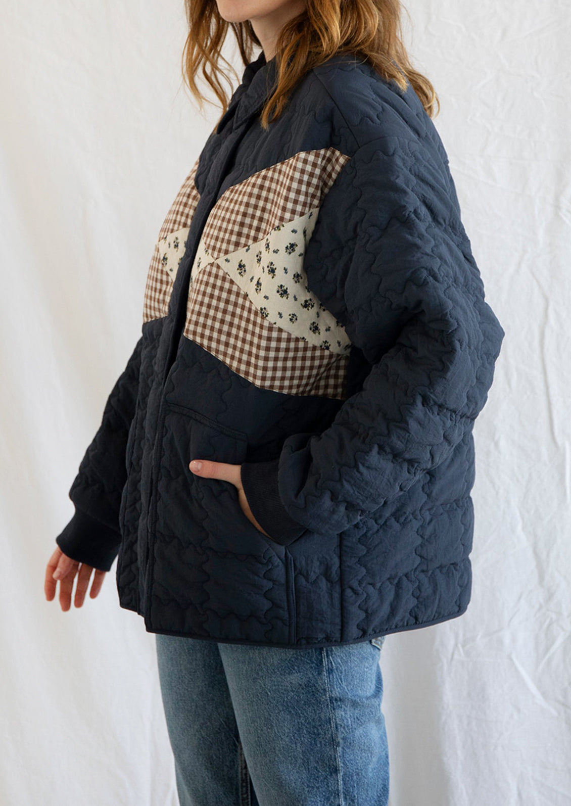 A woman wearing a navy blue jacket with squiggle shaped quilting and gingham and floral patchwork detailing at front.