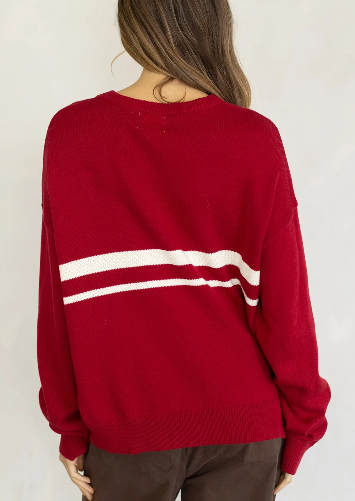 A person wearing a long sleeve cotton sweater in red with two white stripes at middle chest.