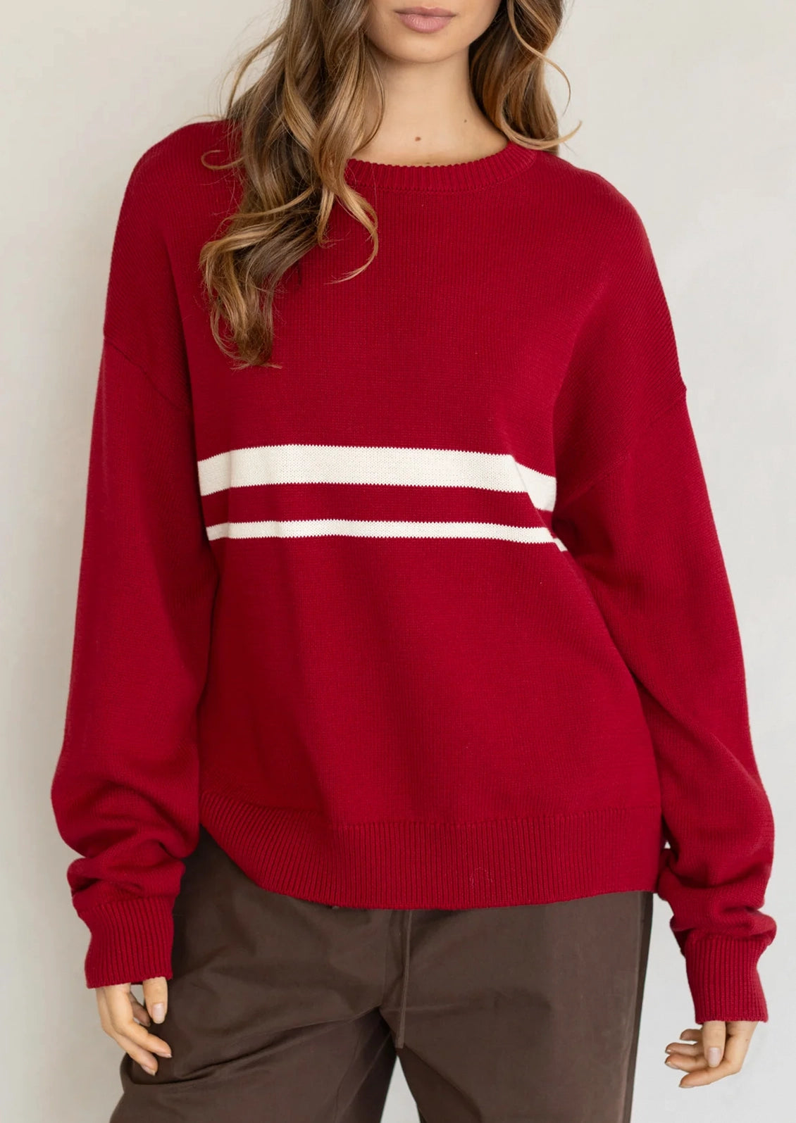 A person wearing a long sleeve cotton sweater in red with two white stripes at middle chest.