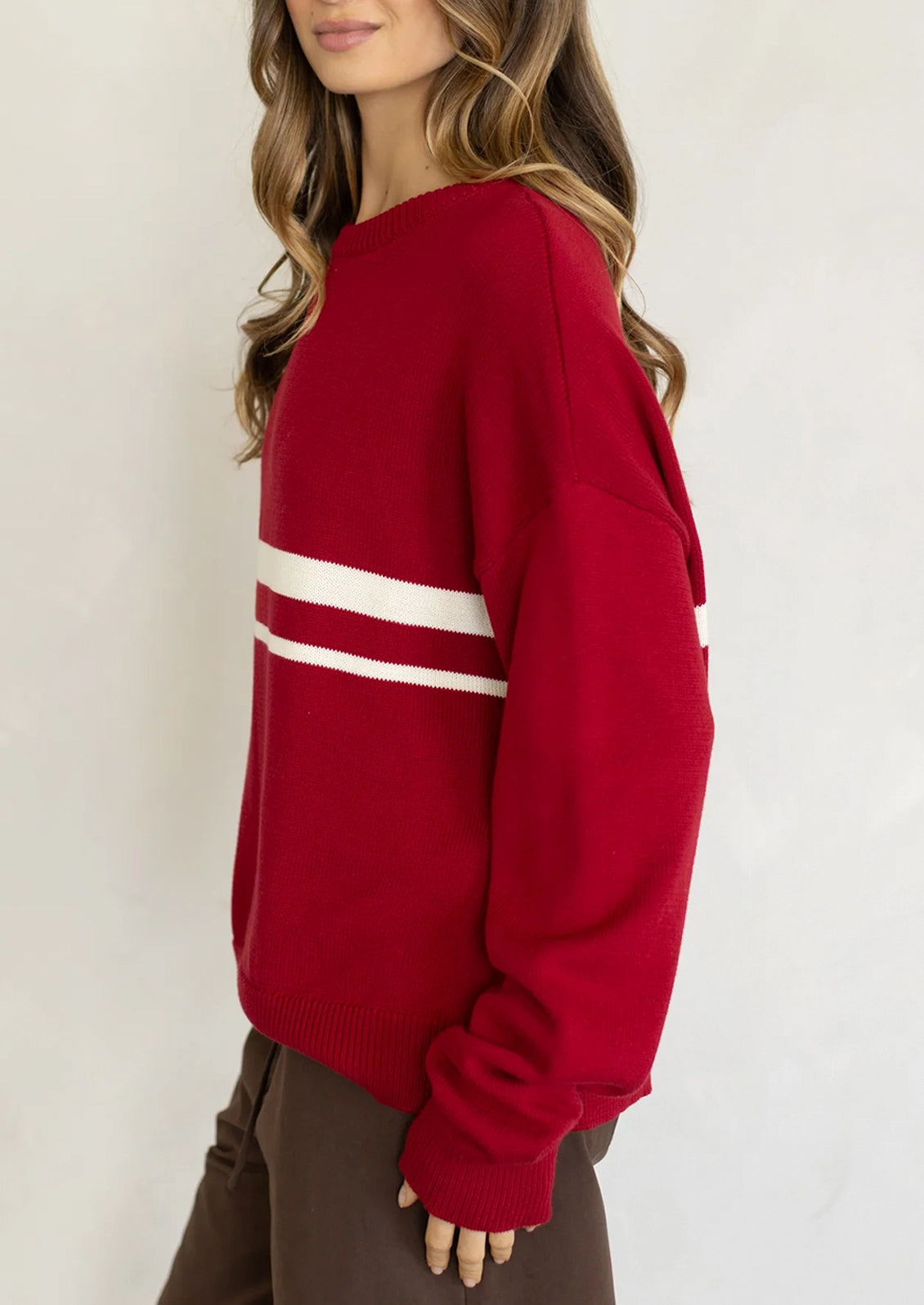 A person wearing a long sleeve cotton sweater in red with two white stripes at middle chest.