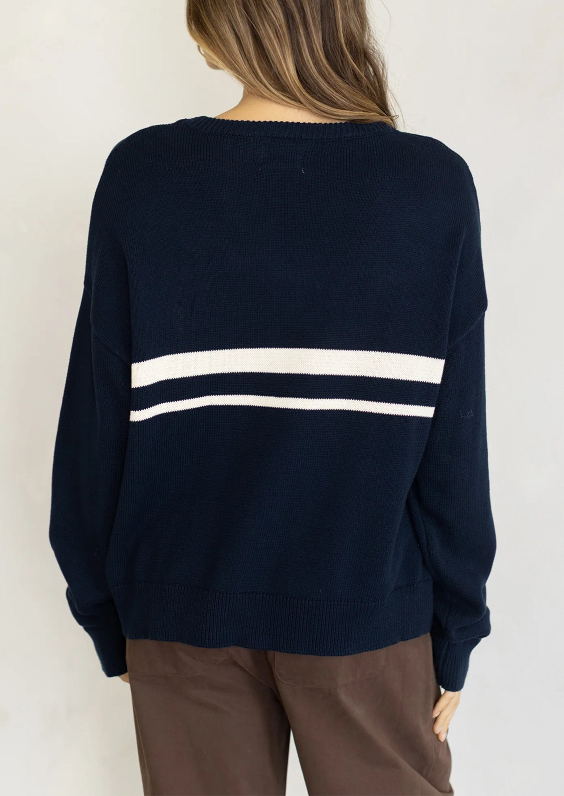 A person wearing a long sleeve cotton sweater in navy with two white stripes at middle chest.