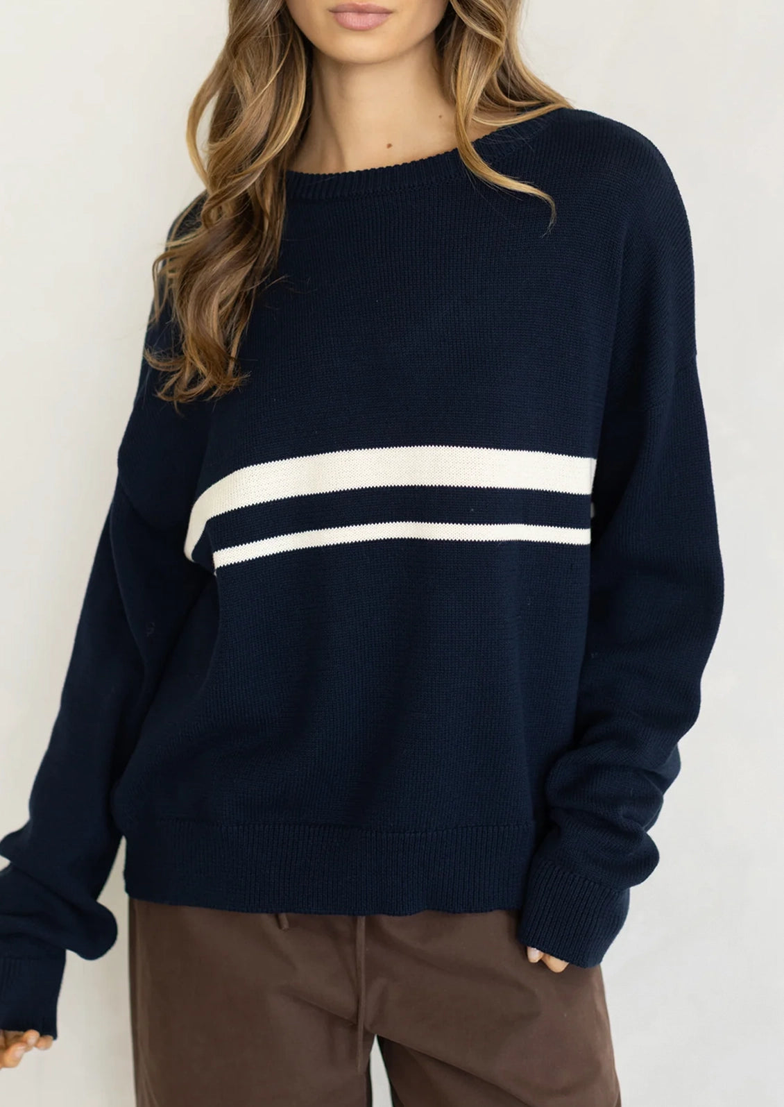 A person wearing a long sleeve cotton sweater in navy with two white stripes at middle chest.
