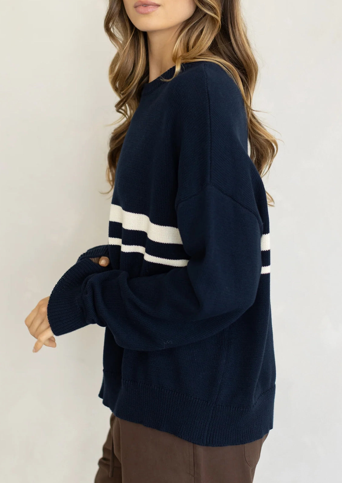 A person wearing a long sleeve cotton sweater in navy with two white stripes at middle chest.