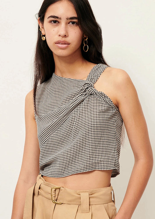 Woman wearing a black and white checkered top with beige pants on a light background