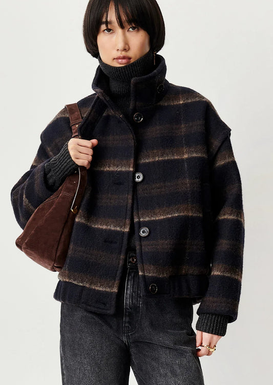 A woman wearing a navy blue and brown plaid short jacket with funnel neck and button front.