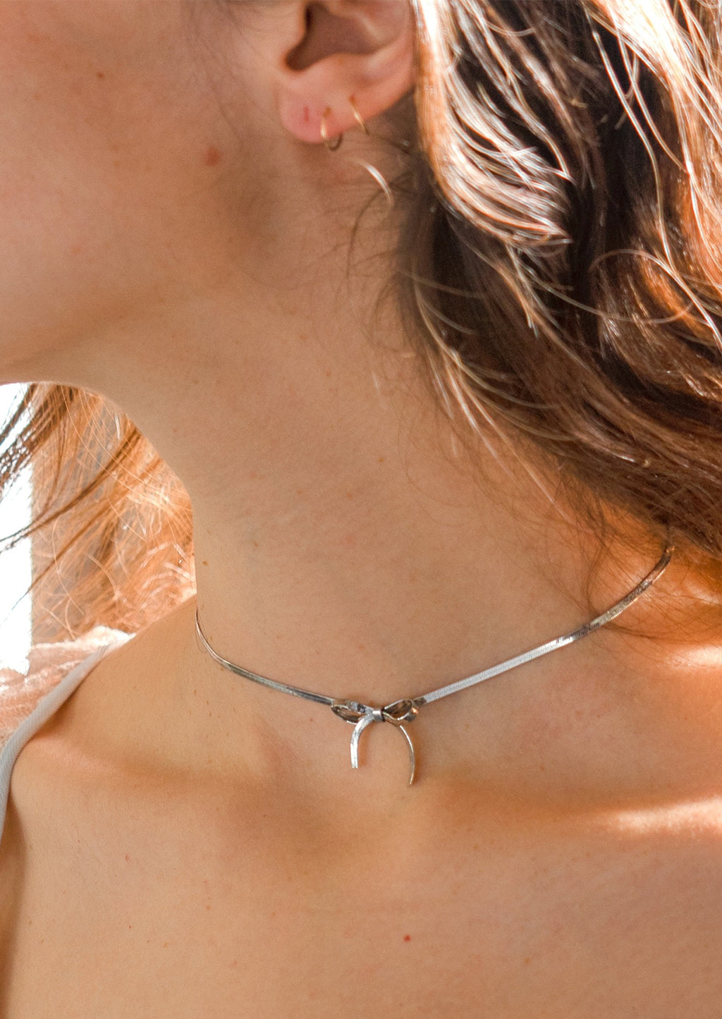 Silver: A woman wearing a silver choker-style necklace with bow shape at front.