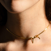 Gold: A woman wearing a gold choker-style necklace with bow shape at front.