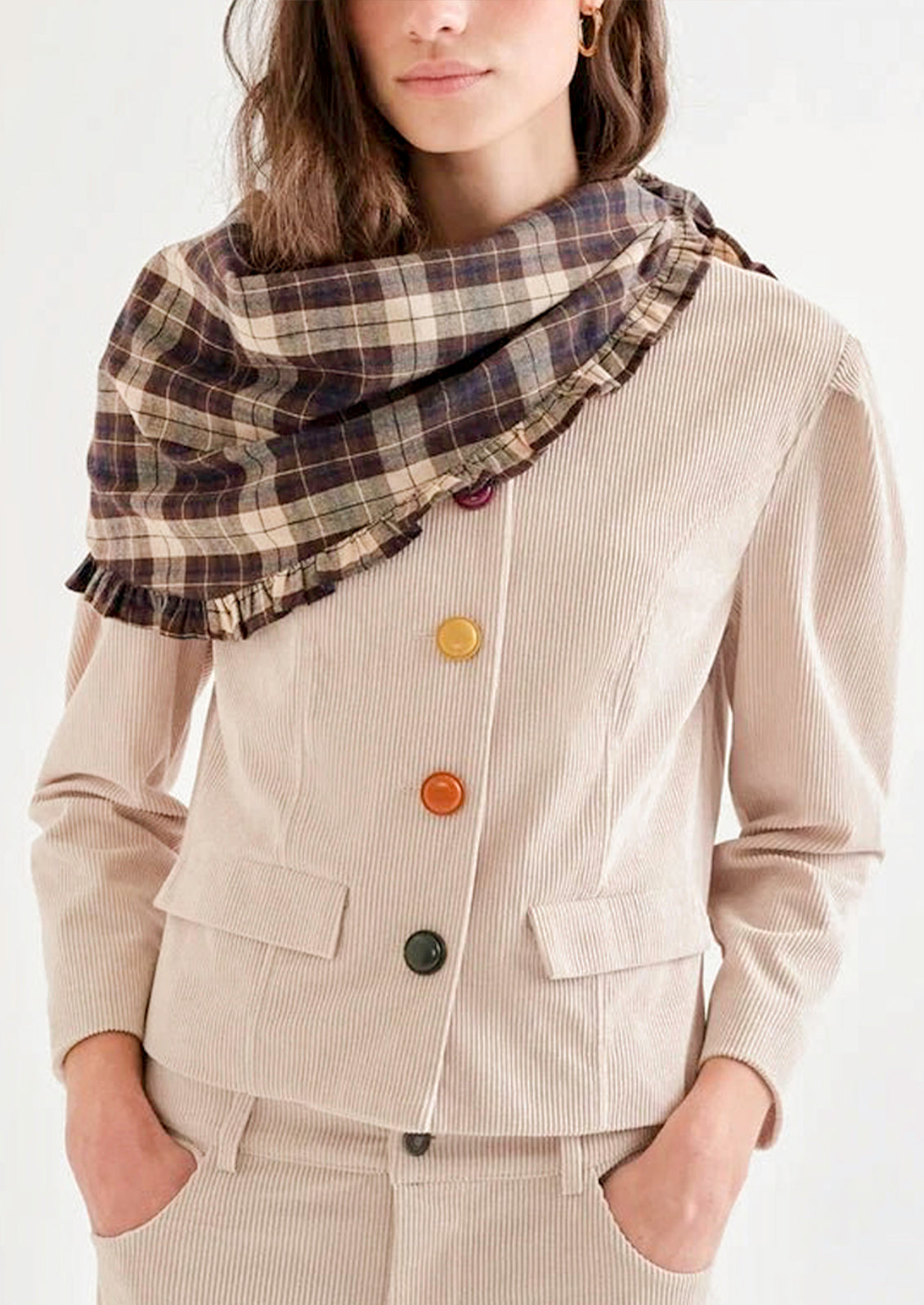 A woman wearing a brown plaid bandana with a ruffled trim draped over her shoulders.