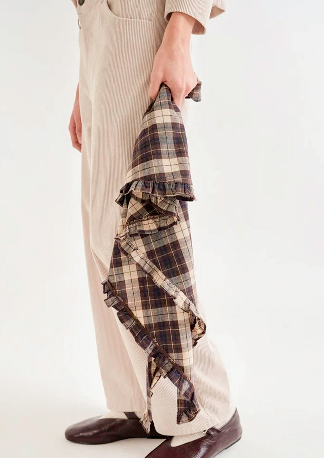A woman holding a brown plaid bandana with a ruffled trim against her body.