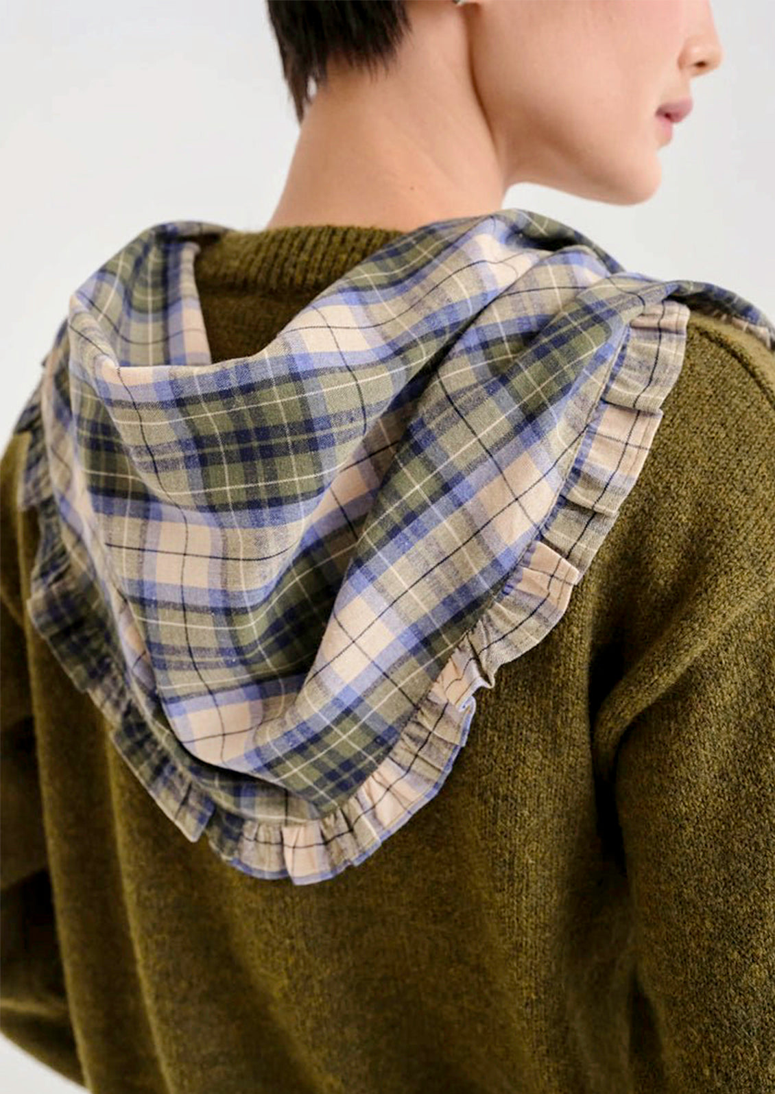A woman wearing a green, blue, and tan plaid bandana with a ruffled trim draped over her shoulders.