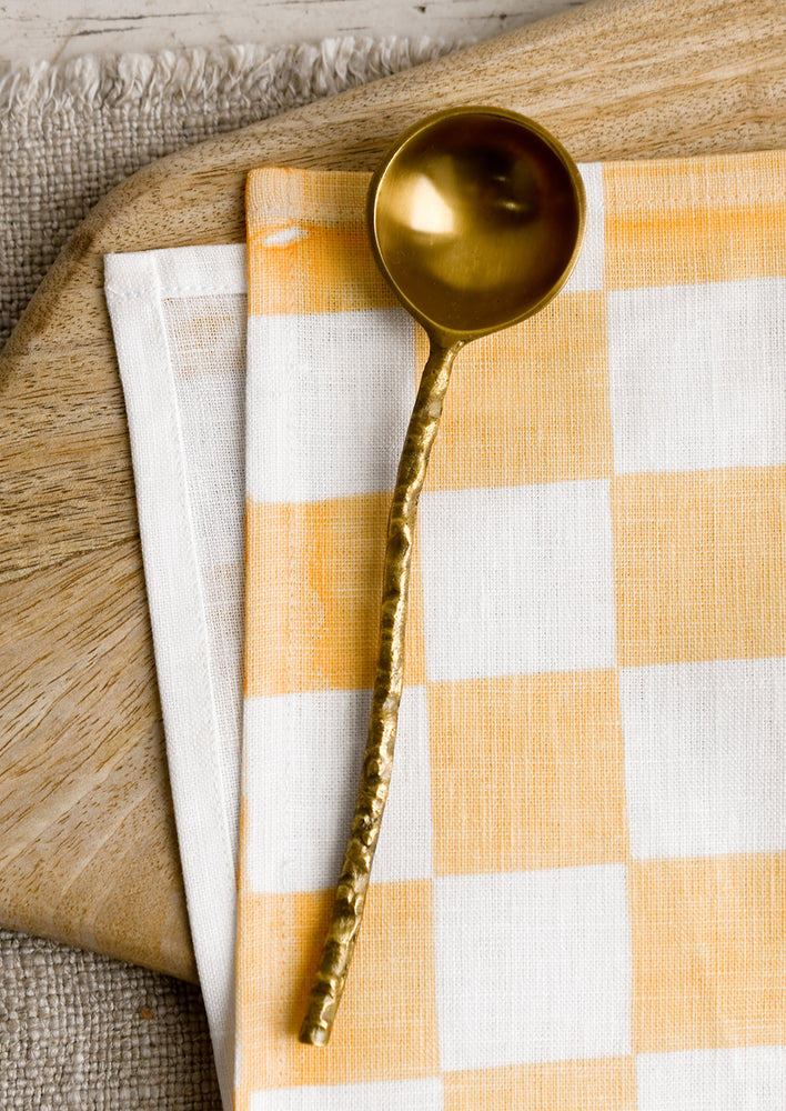 1: A brass spoon with textured organic shaped handle.