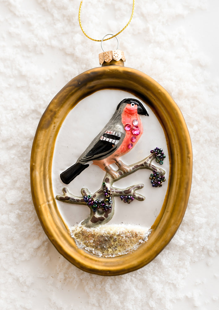 A glass ornament of gold frame around red bird.