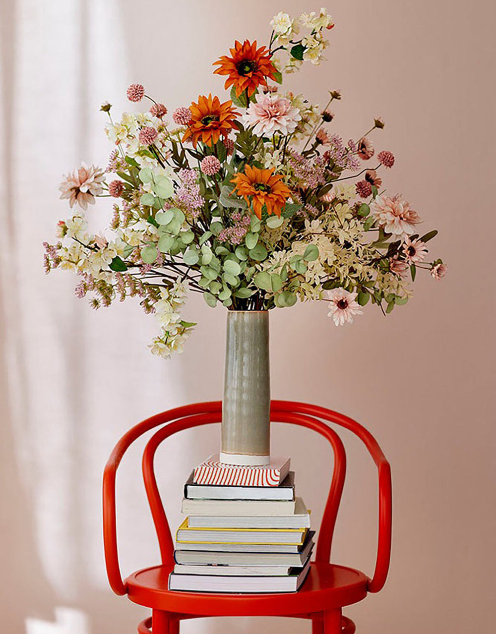 A vase of faux flowers sitting on a stack of books on a chair.