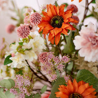 2: A faux flower arrangement with pink flowers and orange sunflowers.
