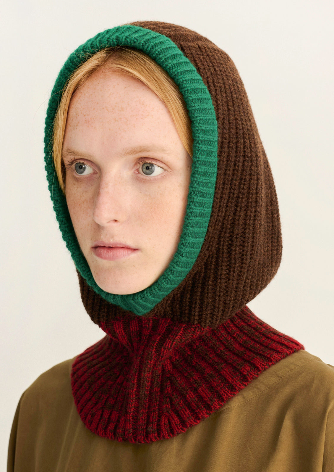 A woman wearing a brown, red, and green color block balaclava with a ribbed knit design.