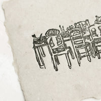 2: An art print made from grey handmade paper with letterpressed image of a dining table with chairs.