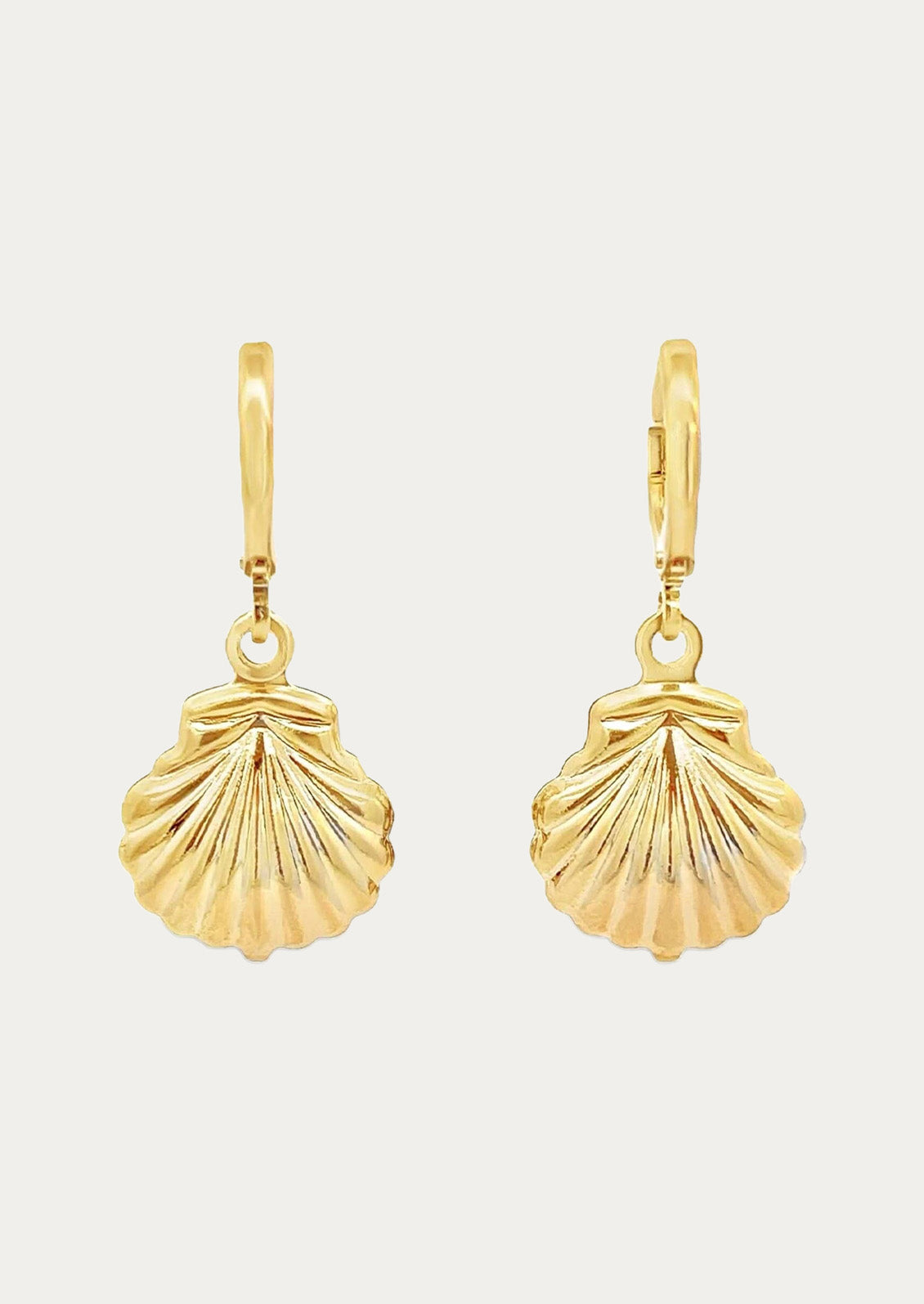 A pair of gold huggie hoop earrings with gold dangling seashell charms on a white background.