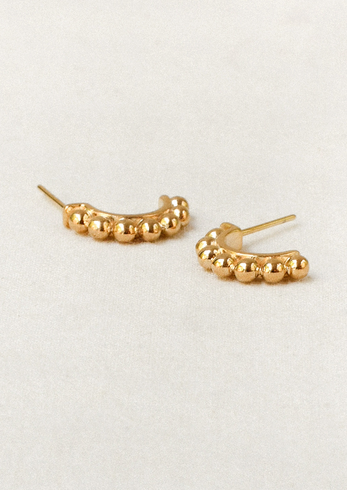 A pair of gold half hoop earrings with a beaded ball design along the tops.