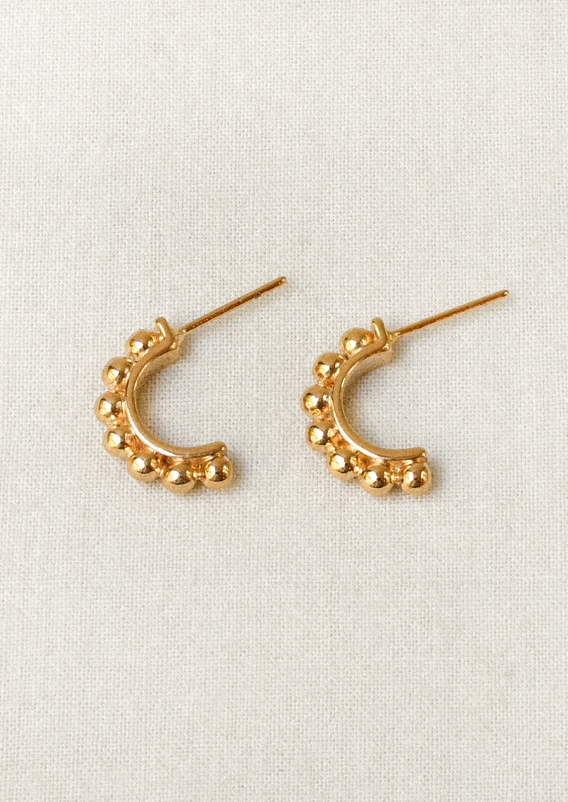 A pair of gold half hoop earrings with a beaded ball design along the tops.