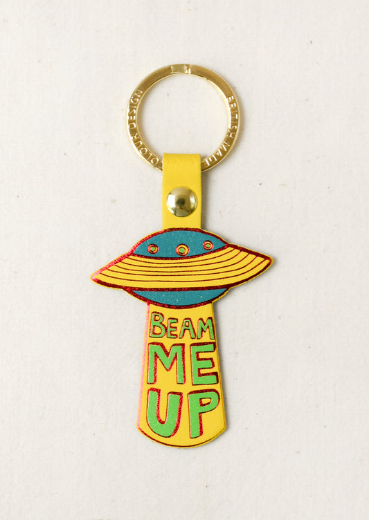 A leather keychain in the shape of a UFO with the words "Beam Me Up" on the front. Attached to a gold keyring.