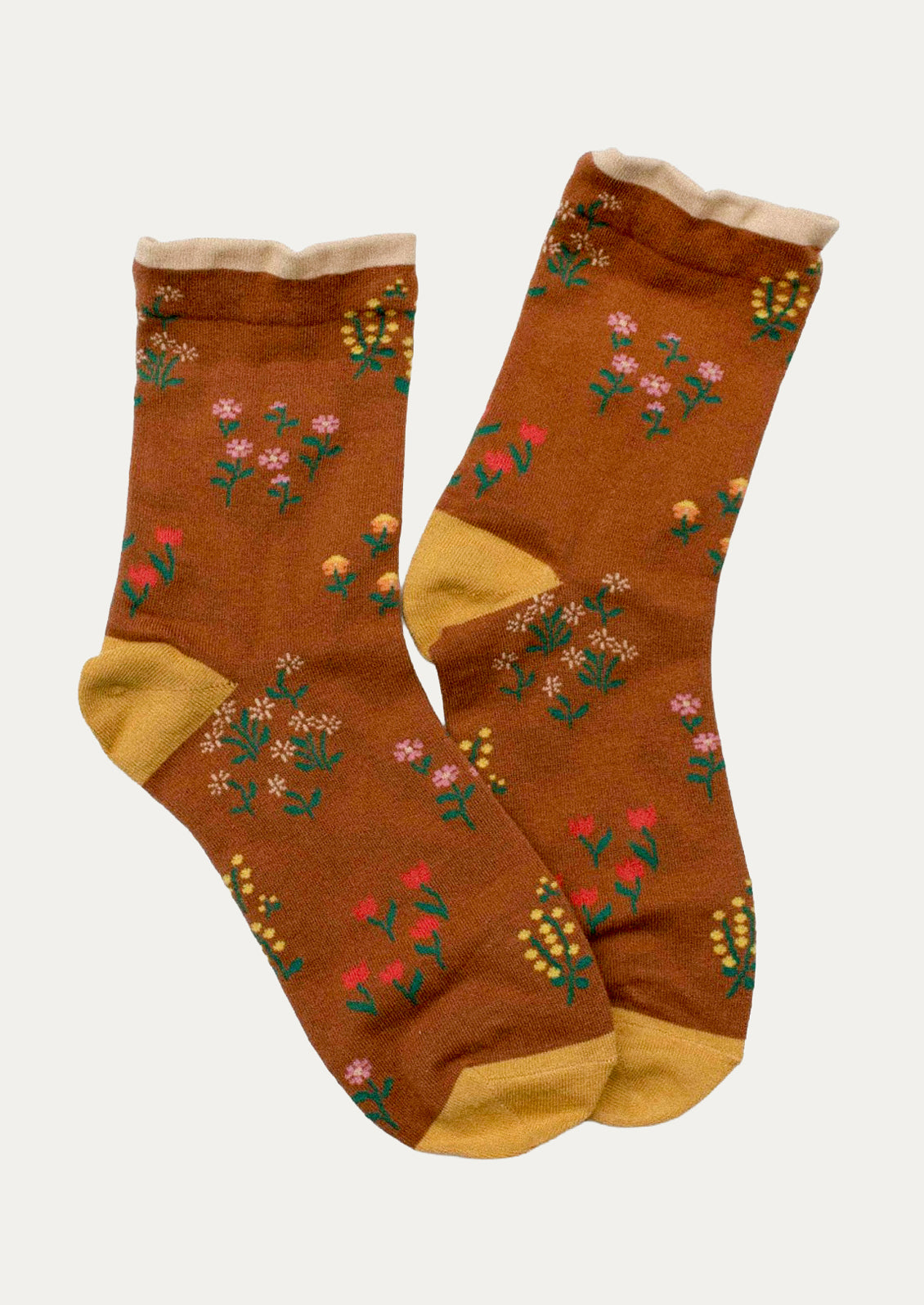 A pair of brown crew socks with a colorful floral pattern and mustard yellow heels, toes, and cuffs, displayed against a light gray background.