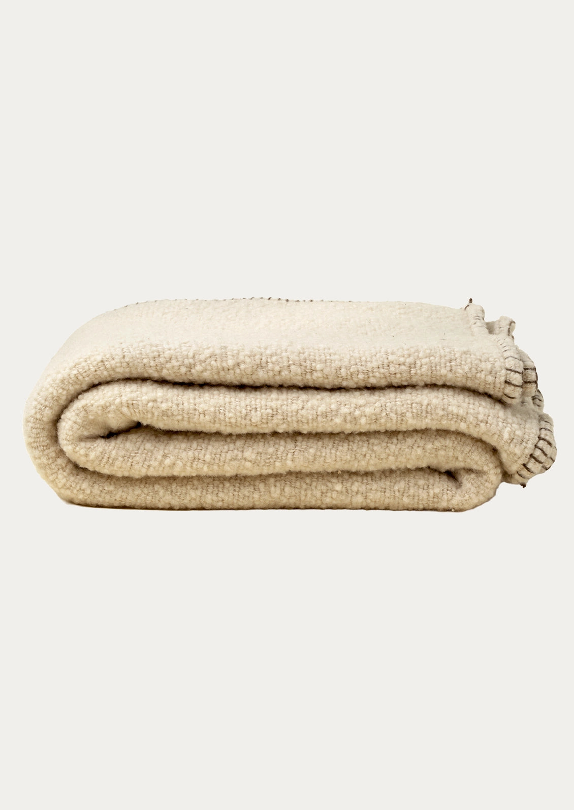 A folded beige textured throw blanket with a whipstitched border in brown.