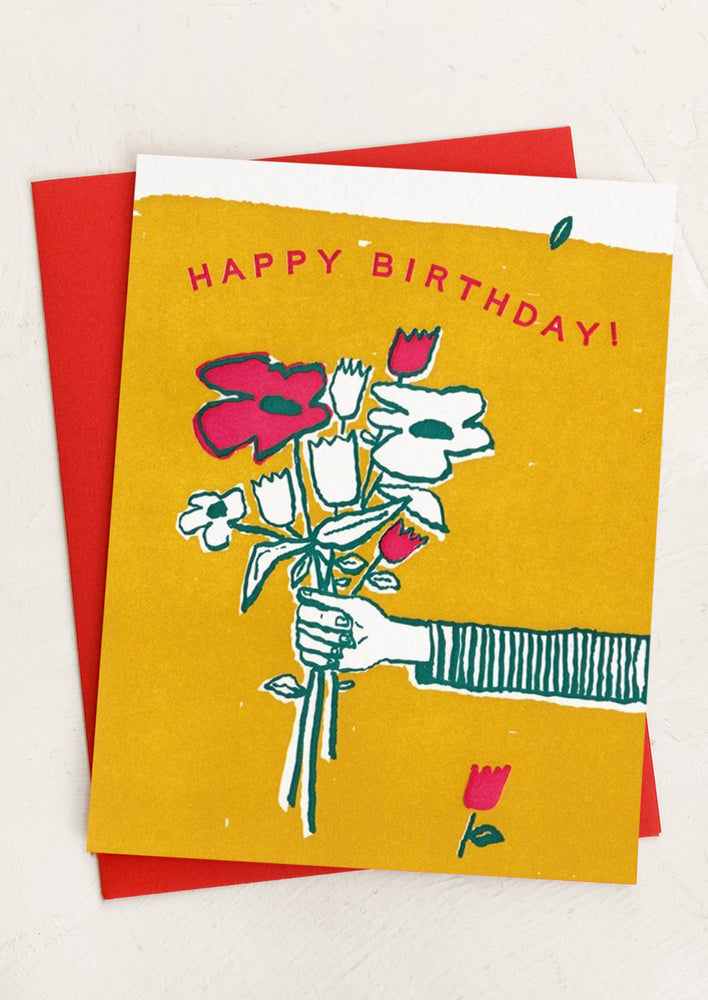 A letterpressed birthday card with image of human hand holding a bouquet of flowers.