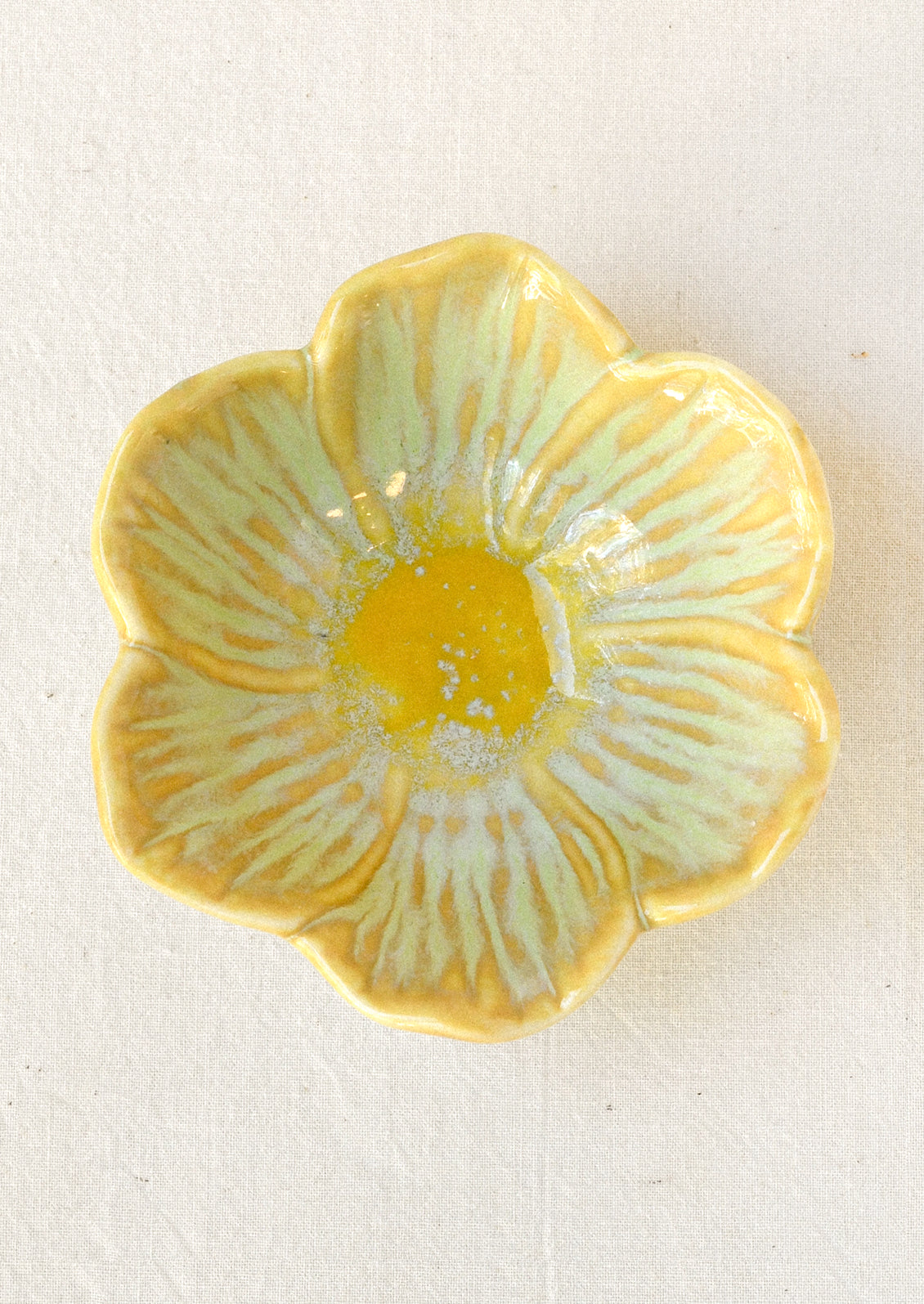 A small ceramic catchall bowl in the shape of a six petal flower in sage green with a yellow center.
