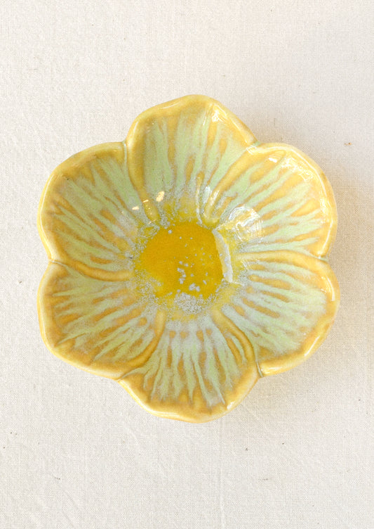 A small ceramic catchall bowl in the shape of a six petal flower in sage green with a yellow center.