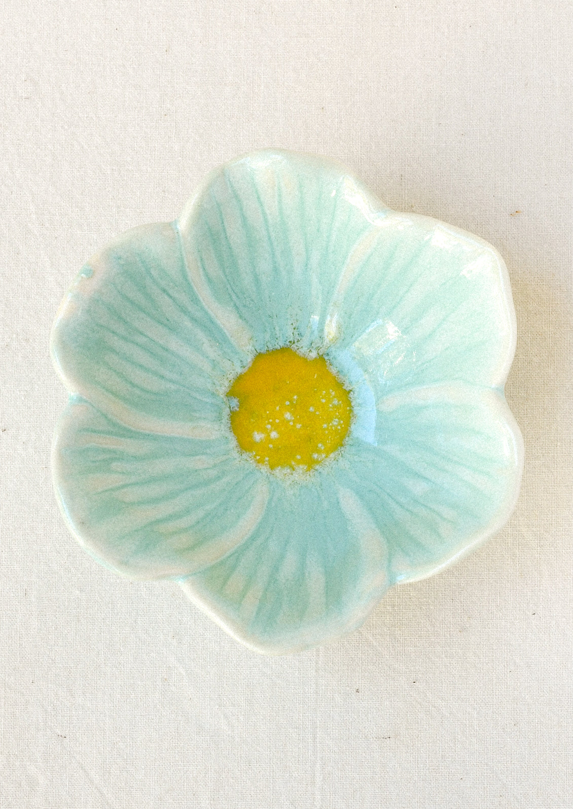 A small ceramic catchall bowl in the shape of a six petal flower in sky blue with a yellow center.