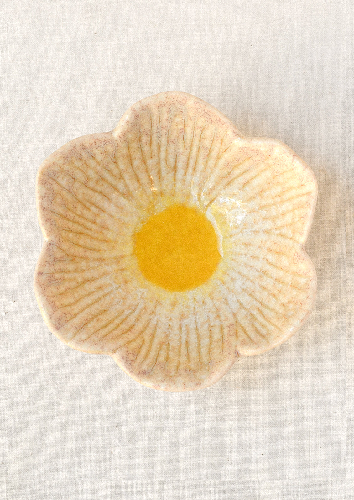 A small ceramic catchall bowl in the shape of a six petal flower in a cream color with a yellow center.