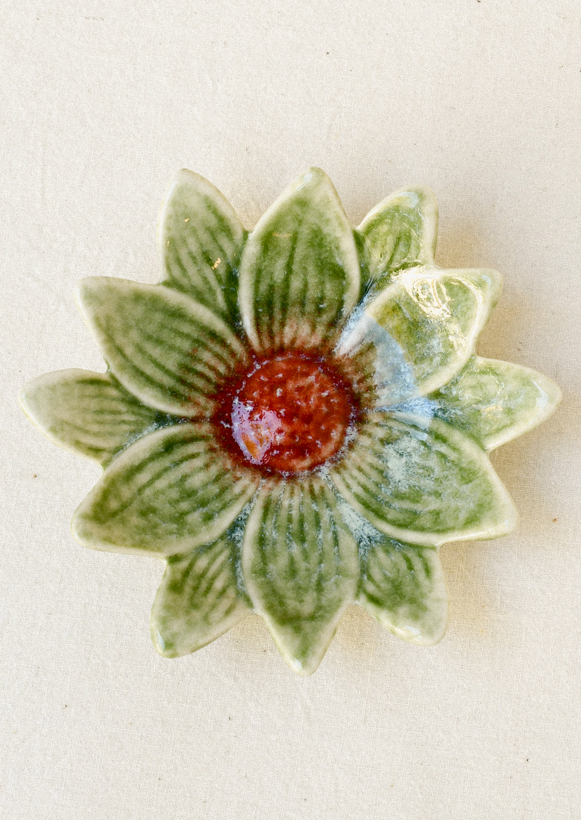 A small ceramic catchall dish in the shape of a flower in green with a red center.