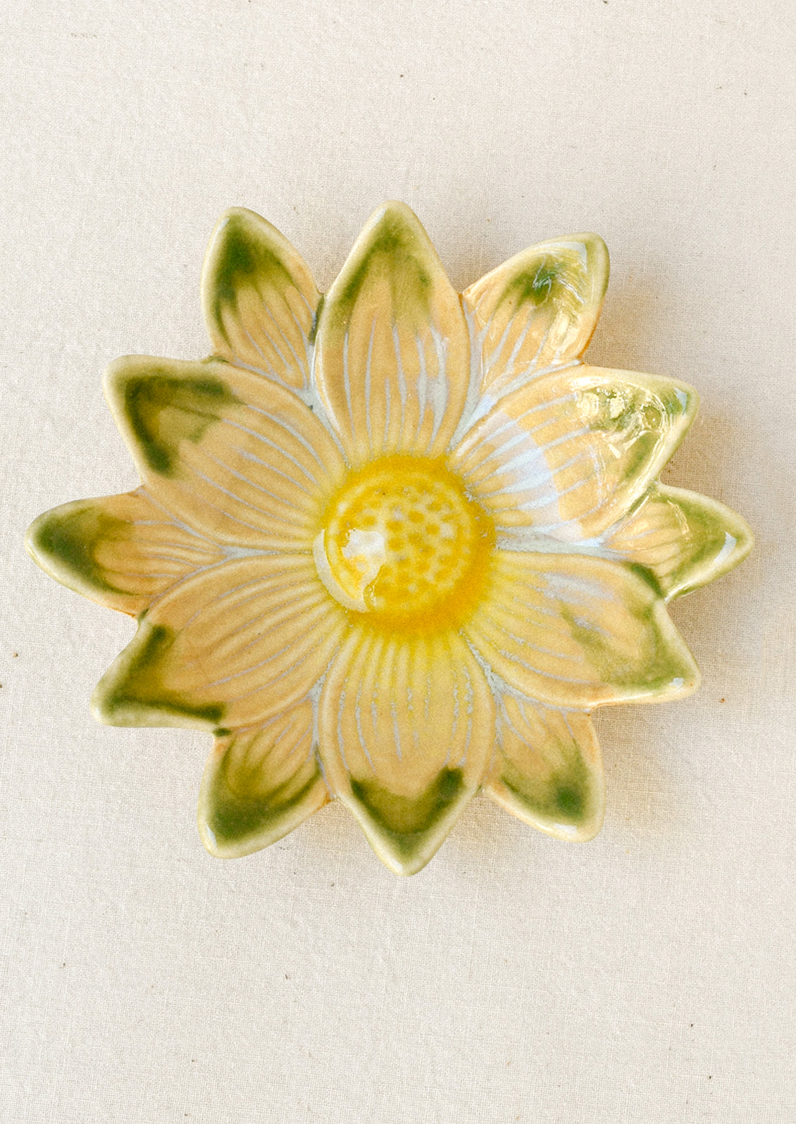 A small ceramic catchall dish in the shape of a flower in green and yellow.