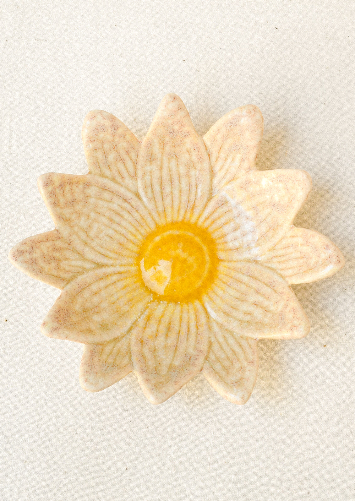 A small ceramic catchall dish in the shape of a flower in cream with a yellow center.