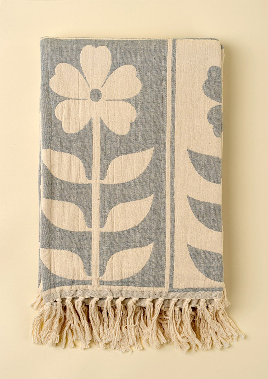 Floral patterned throw in blue and cream with tassel trim.