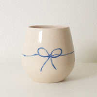 1: A white rounded ceramic cup with hand painted blue bow.