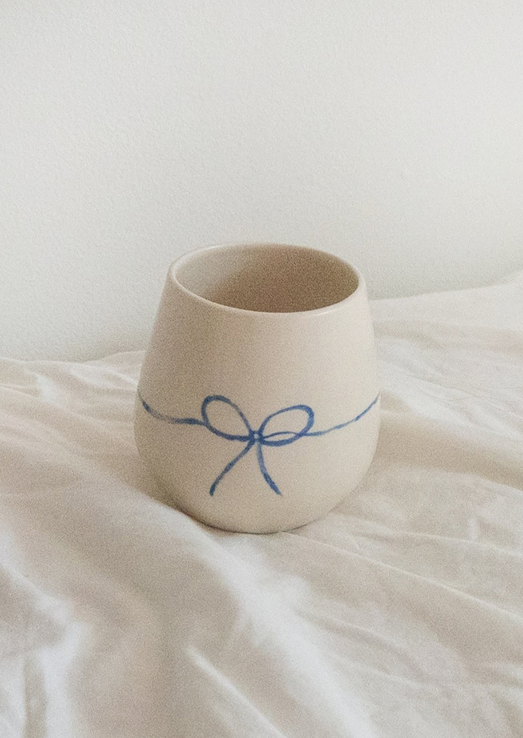 2: A white rounded ceramic cup with hand painted blue bow.