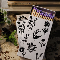 1: A matchbox in white with black botanical print, housing purple tipped matches.