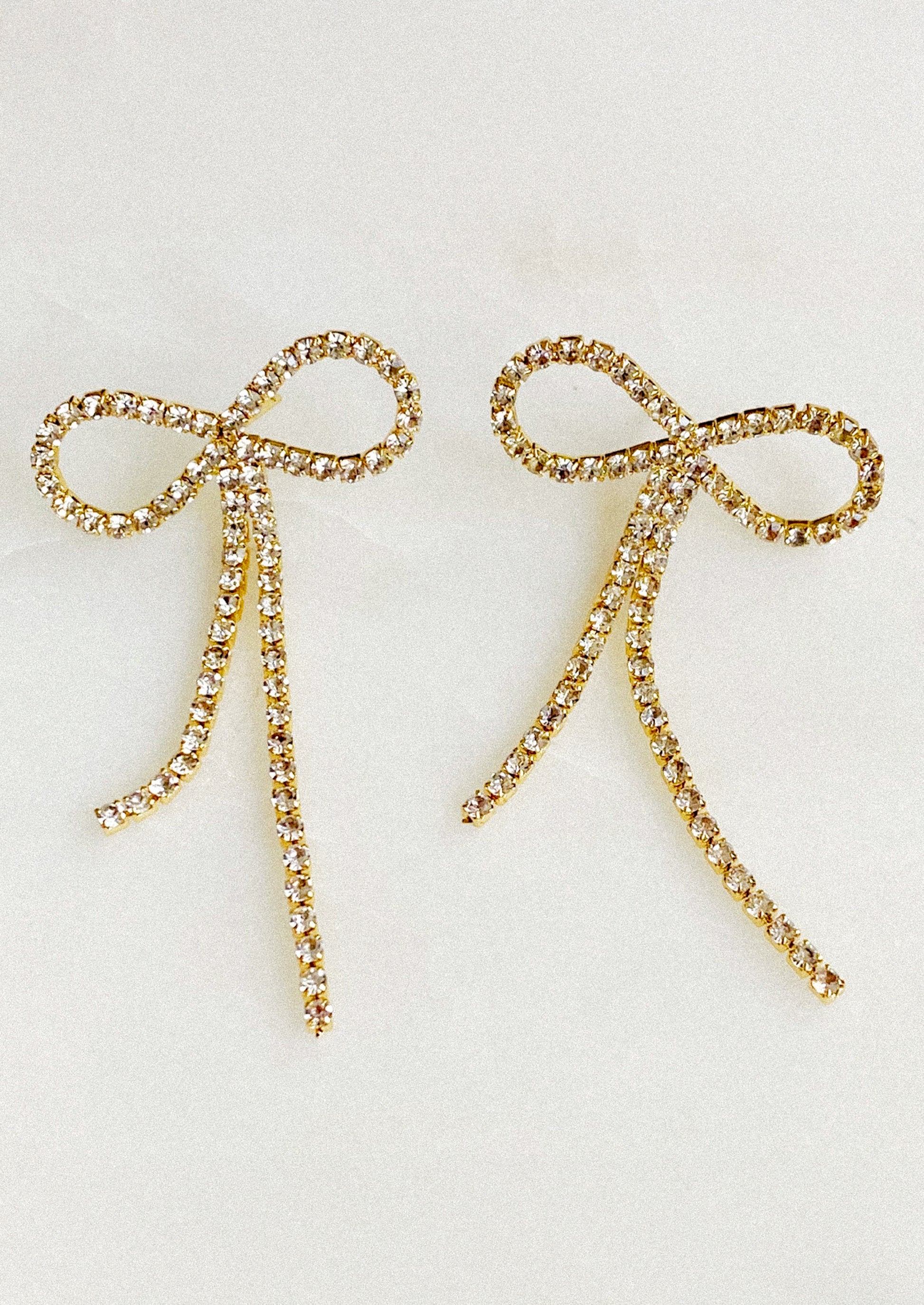Gold bow-shaped earrings with rhinestones on a light gray background