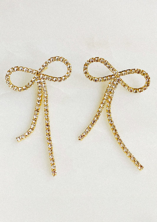 Gold bow-shaped earrings with rhinestones on a light gray background