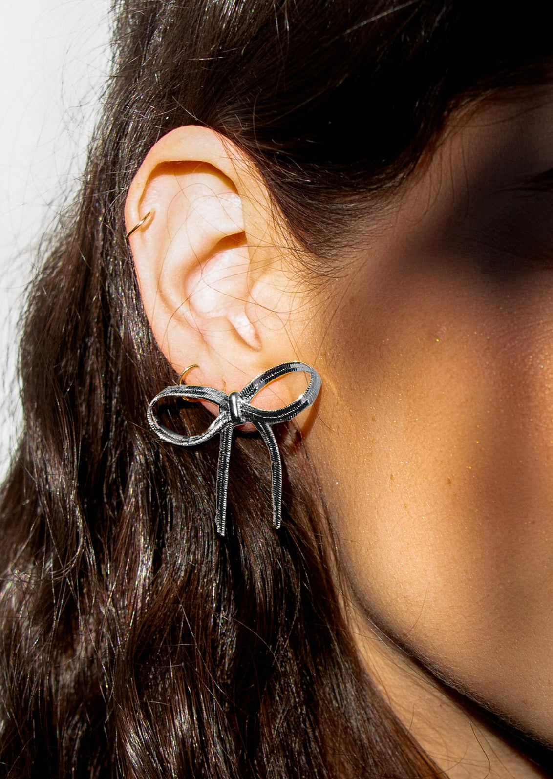 A bow shaped earring made of silver snake chain material.