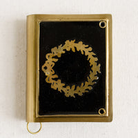 Brass Book: A book-shaped measuring tape with brass wreath design on black enamel.