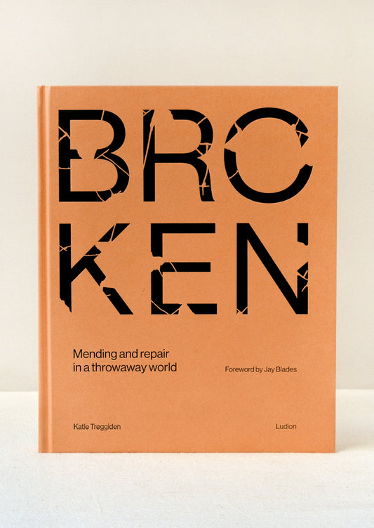 A hardcover orange book with the title "BROKEN" in large broken black letters standing upright on a table.