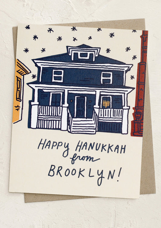 A greeting card with illustration of a house with a menorah in the window, text reads "Happy Hanukkah from Brooklyn!".