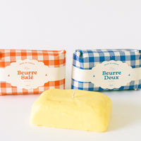 1: A candle in the shape of a block of butter, gingham packaging in red or blue.