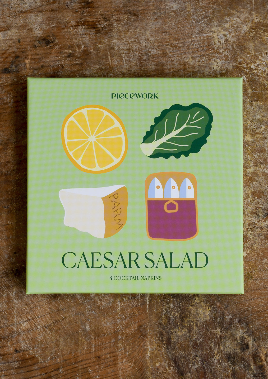 Pack of Caesar Salad cocktail napkins with lemon, romaine, and Parmesan icons on a wooden surface.