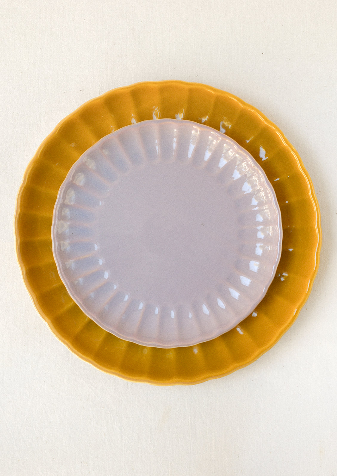 Mustard yellow and lavender ceramic plates stacked together, both with scalloped edges and glossy finishes.