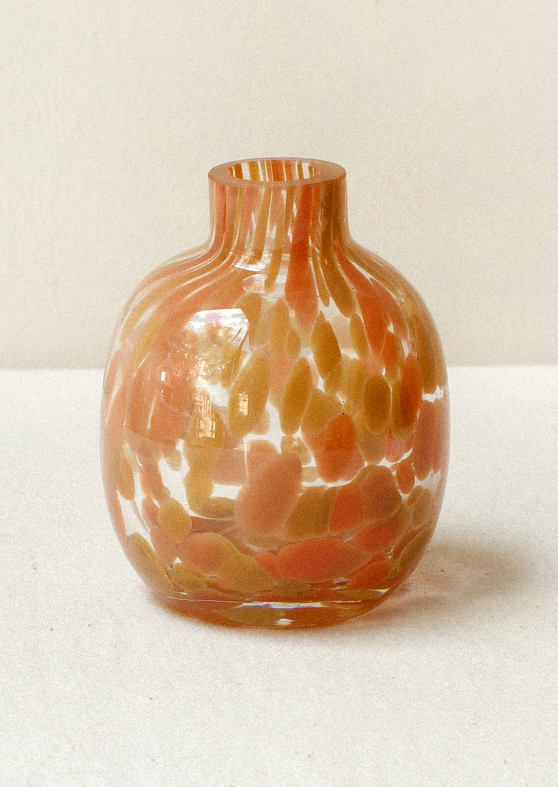 A small glass bud vase with an orange and camel painted design.