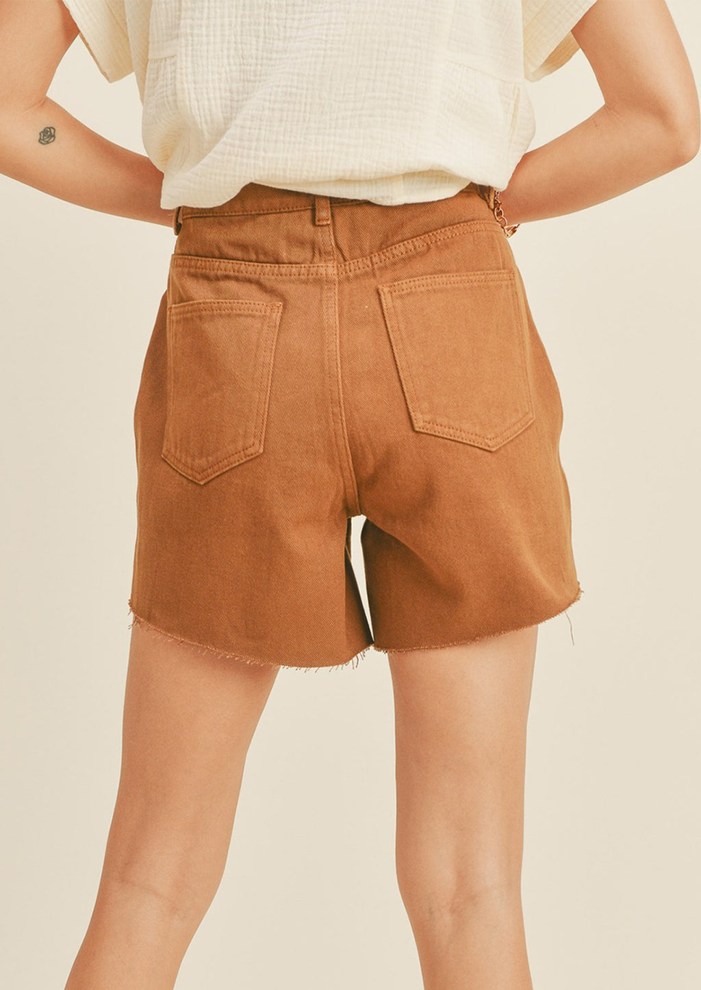 2: A woman in light brown denim shorts, seen from behind. 