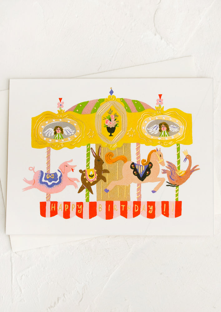 A greeting card with illustration of carousel, text reads "Happy Birthday".